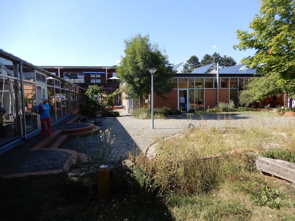 Ein Mann steht auf dem Vorplatz vor Ziegel-Glasfassaden-Gebäuden im Schatten